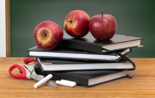 Photo of books and apples on a desk with a chalkboard in the background