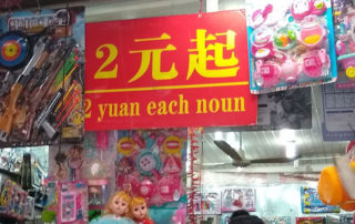 Photo of a sign in China over a display of cheap toys translated in English to "2 yuan each noun"