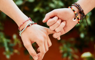 photo of two hands, both with friendship bracelets, holding pinky fingers