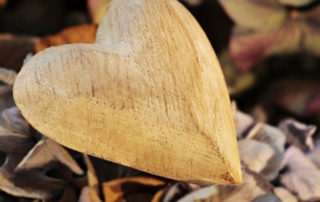 photo of a small wooden heart on a background of dried leaves
