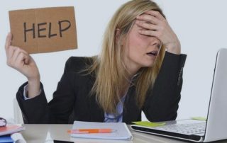Photo of frustrated woman at computer holding hand-lettered sign saying "Help"